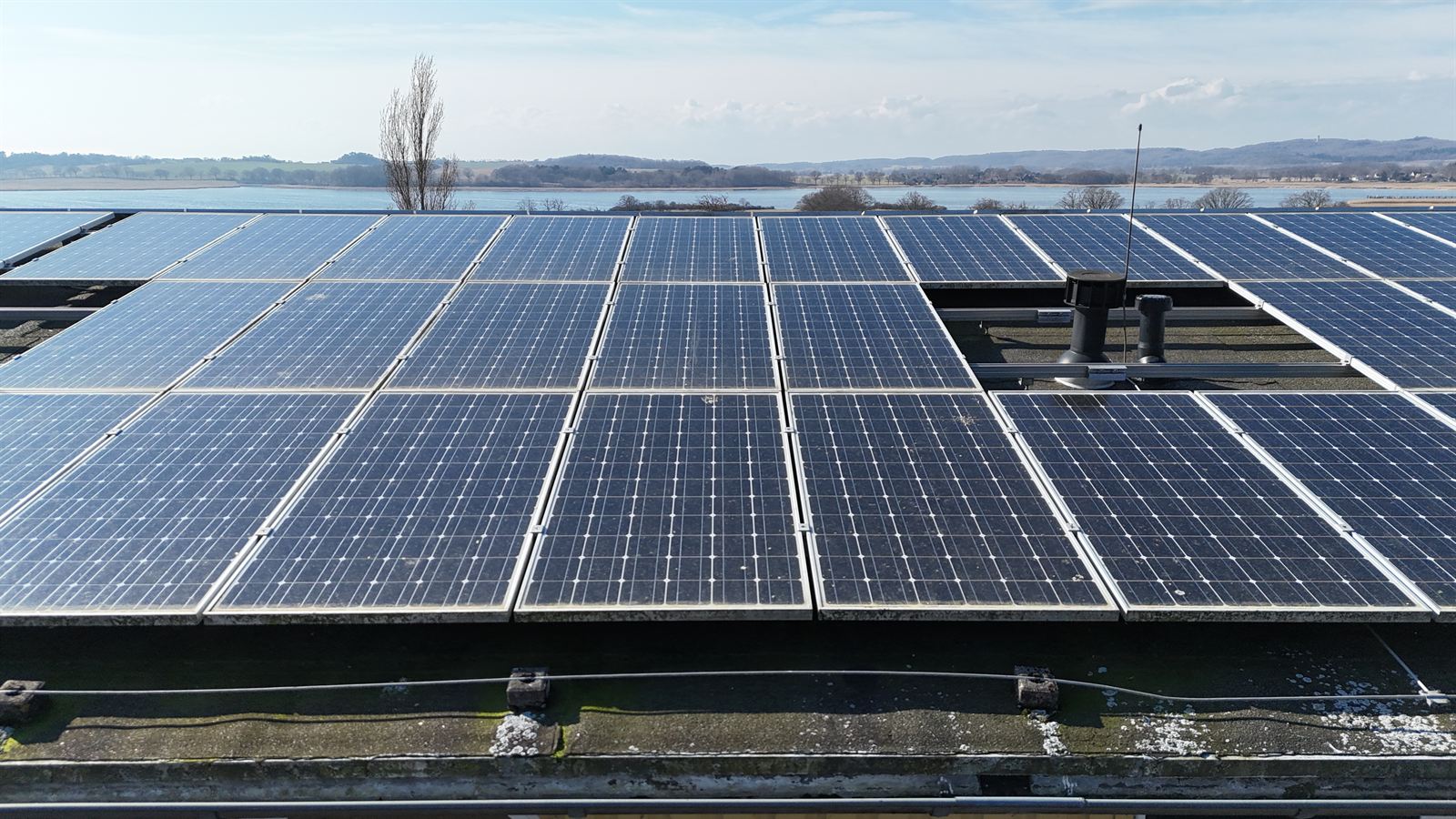Ältere Solaranlage mit blauen Modulen auf einem Flachdach, dahinter der Bodden