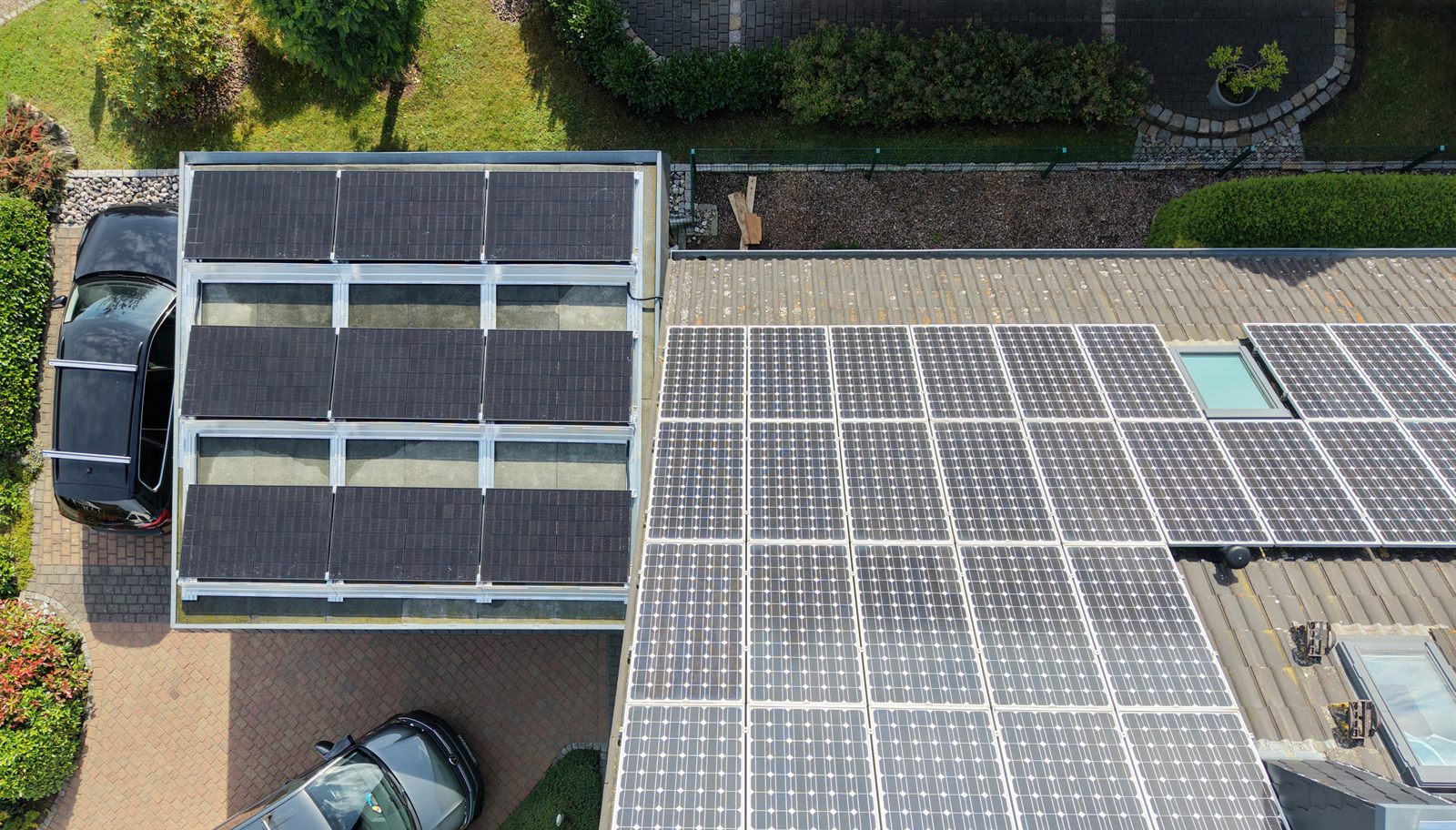 Wohnhaus von oben: ältere blaue Module auf dem Hauptdach, neue schwarze Module auf dem Carport