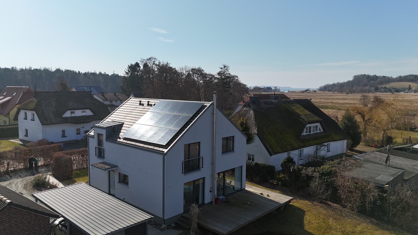 Neubau auf Rügen mit vollflächig belegtem Satteldach, im Hintergrund Reetdächer und offene Landschaft